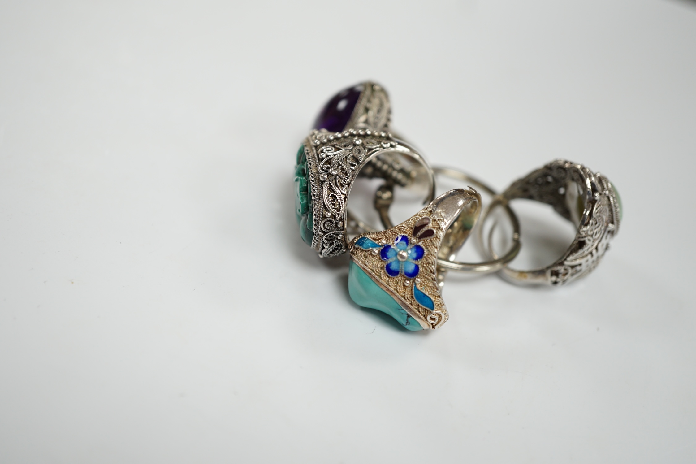 Four assorted Chinese white metal filigree and gem set rings, including turquoise and amethyst.